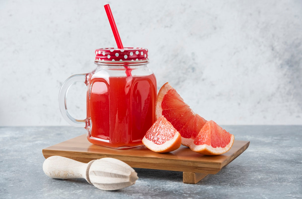 A mason-jar glass of grapefruit juice next to grapefruit slices and a juicer