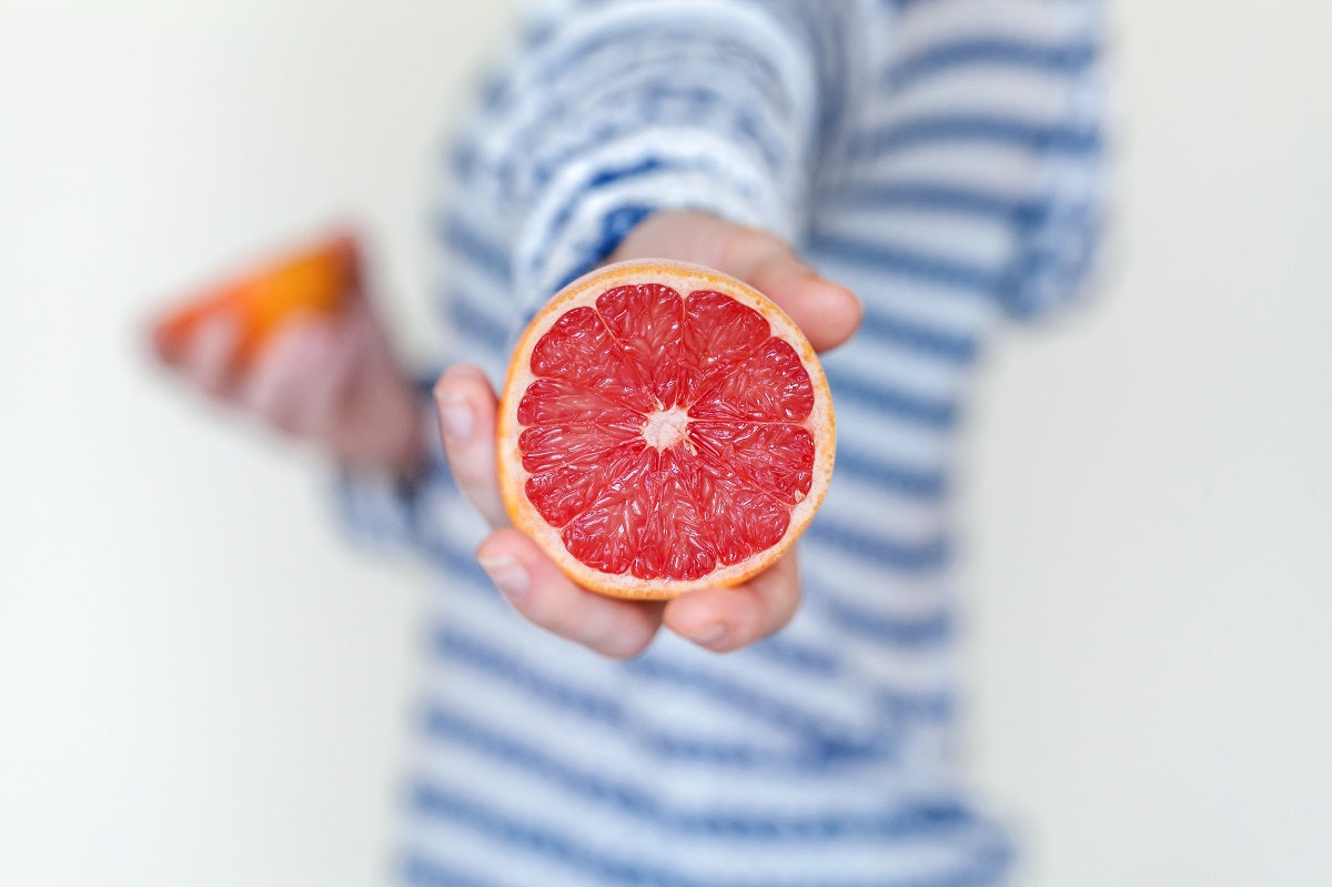 A person holding out a grapefruit half toward the camera