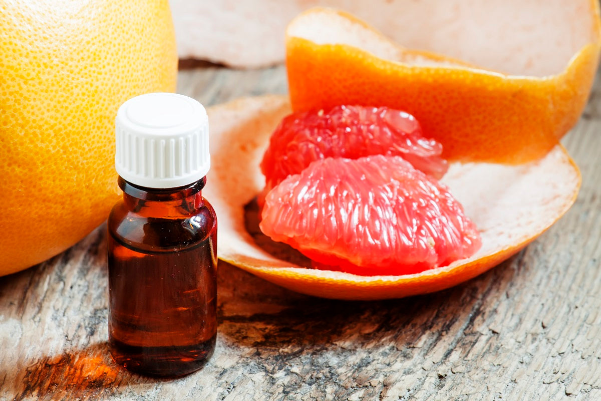 Grapefruit slices and peels next to a small bottle for essential oils