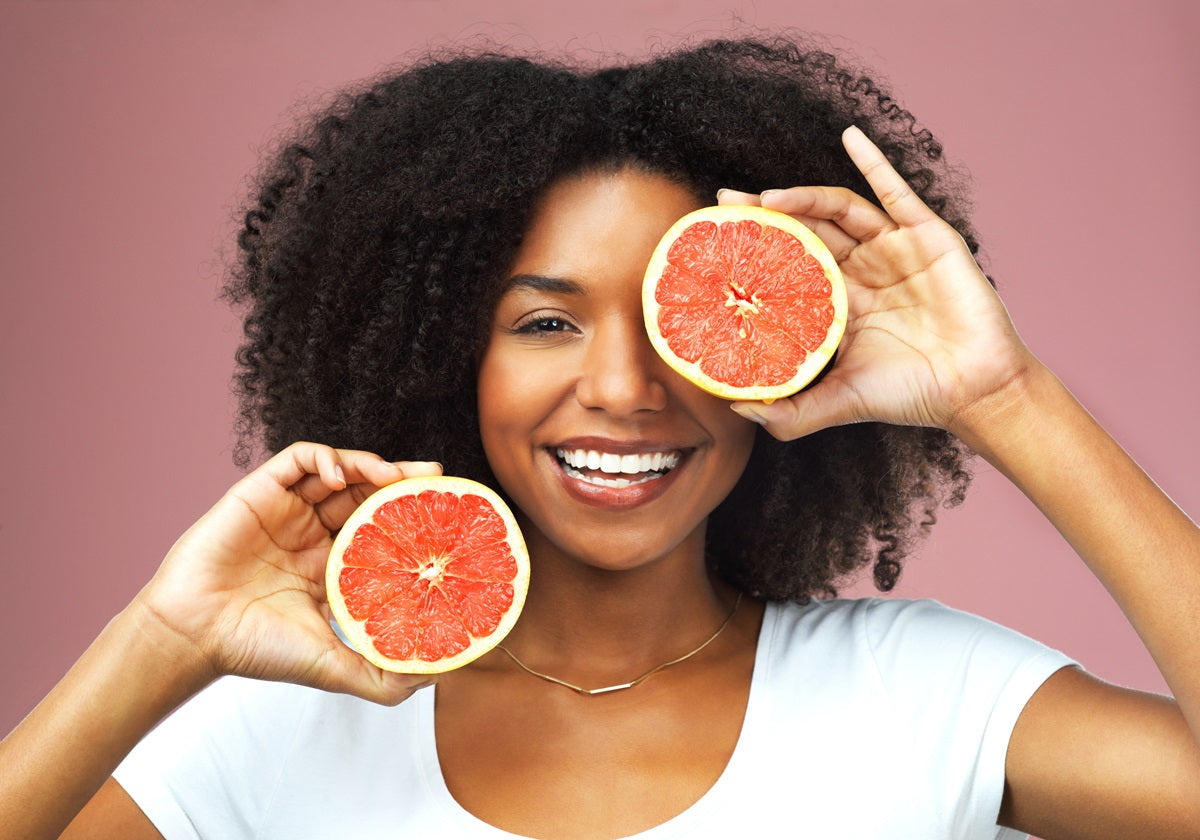 A woman smiling holding two halves of a grapefruit in front of her face