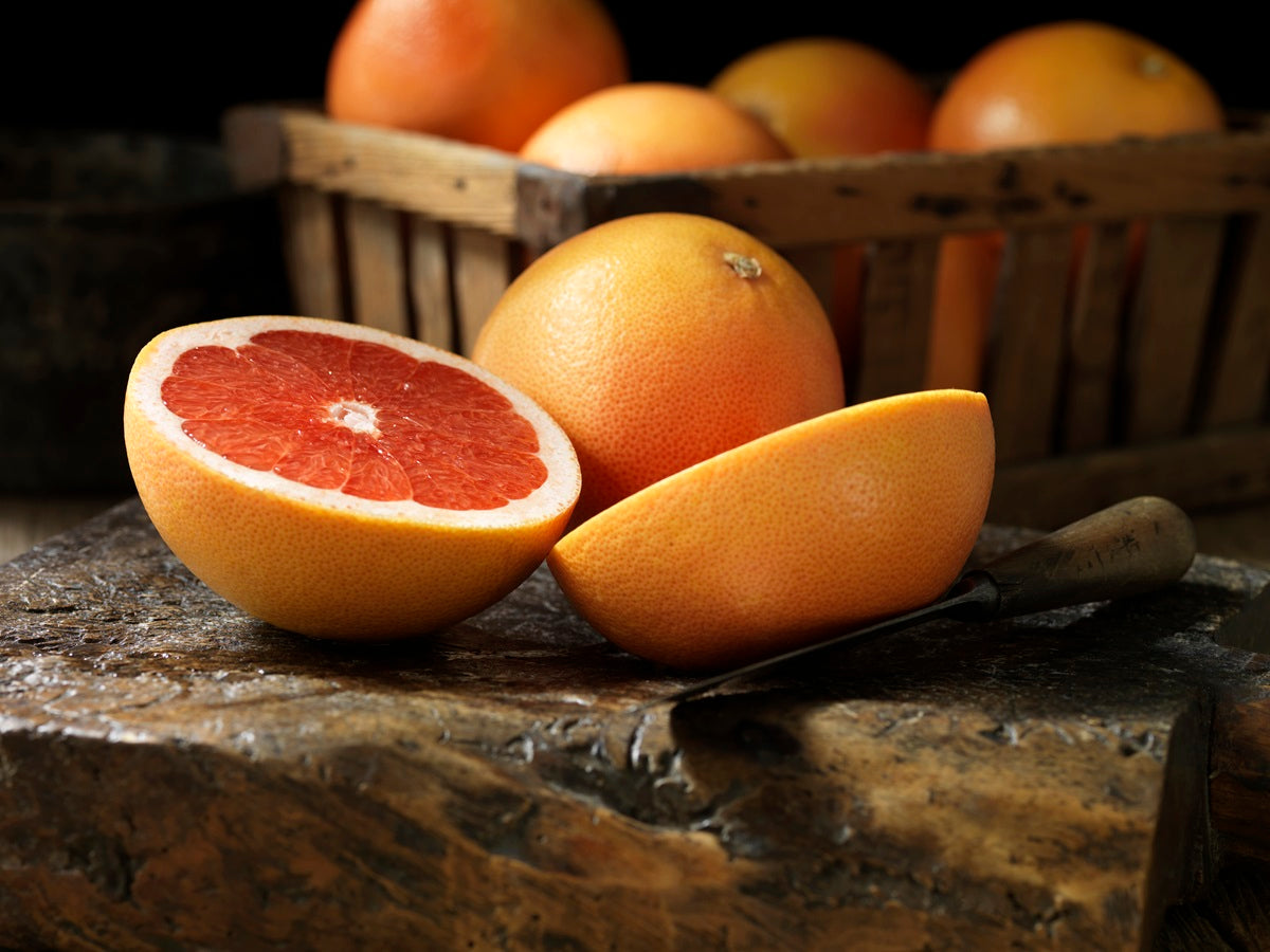 A grapefruit slices in half in front of a basket of grapefruit