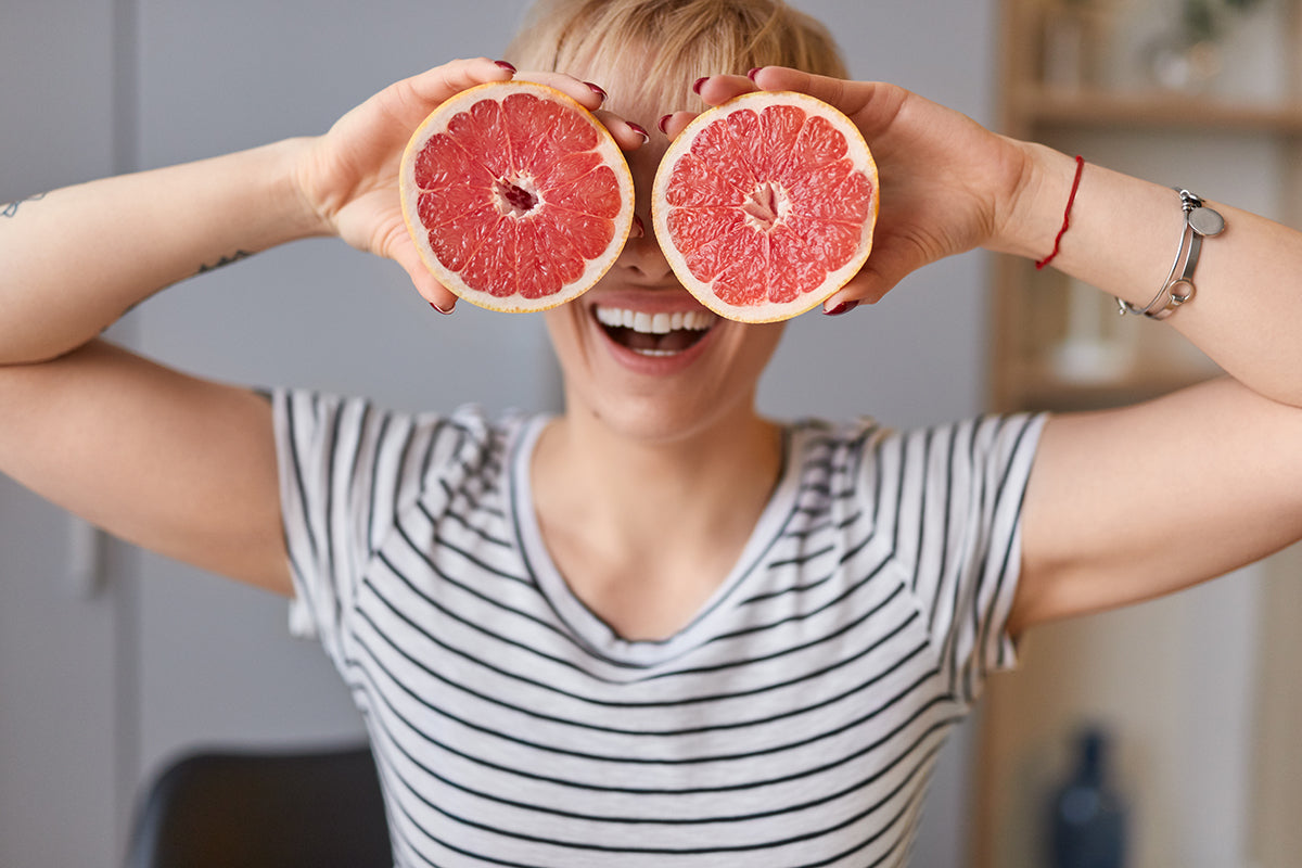 A cheerful woman with two halves of grapefruits in front of her eyes smiling