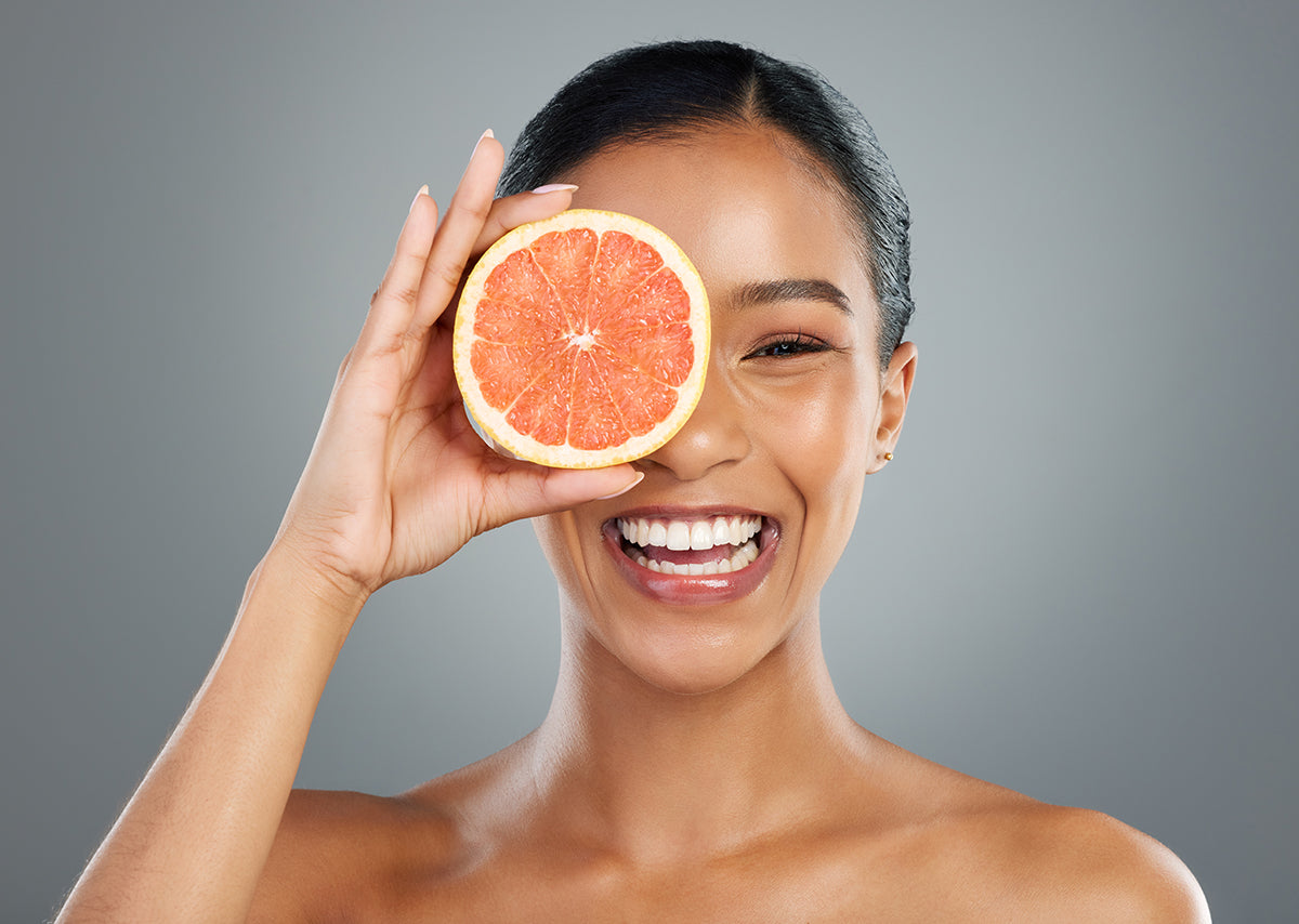 A young woman smiling and holding up half a section of red grapefruit