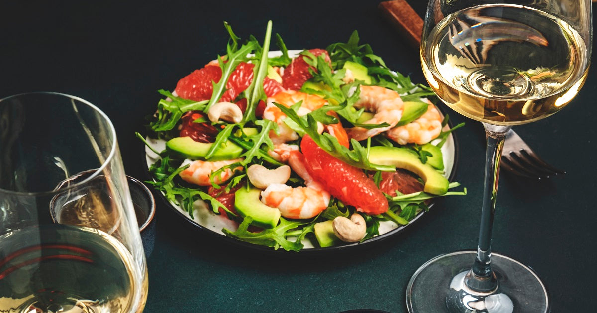 Two plates of grapefruit and shrimp salad on a table with glasses of white wine.