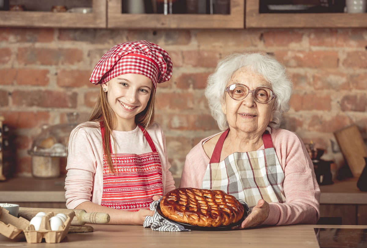 Granddaughter and her granny dressed in aprons smiling at the camera while holding a fruit pie.