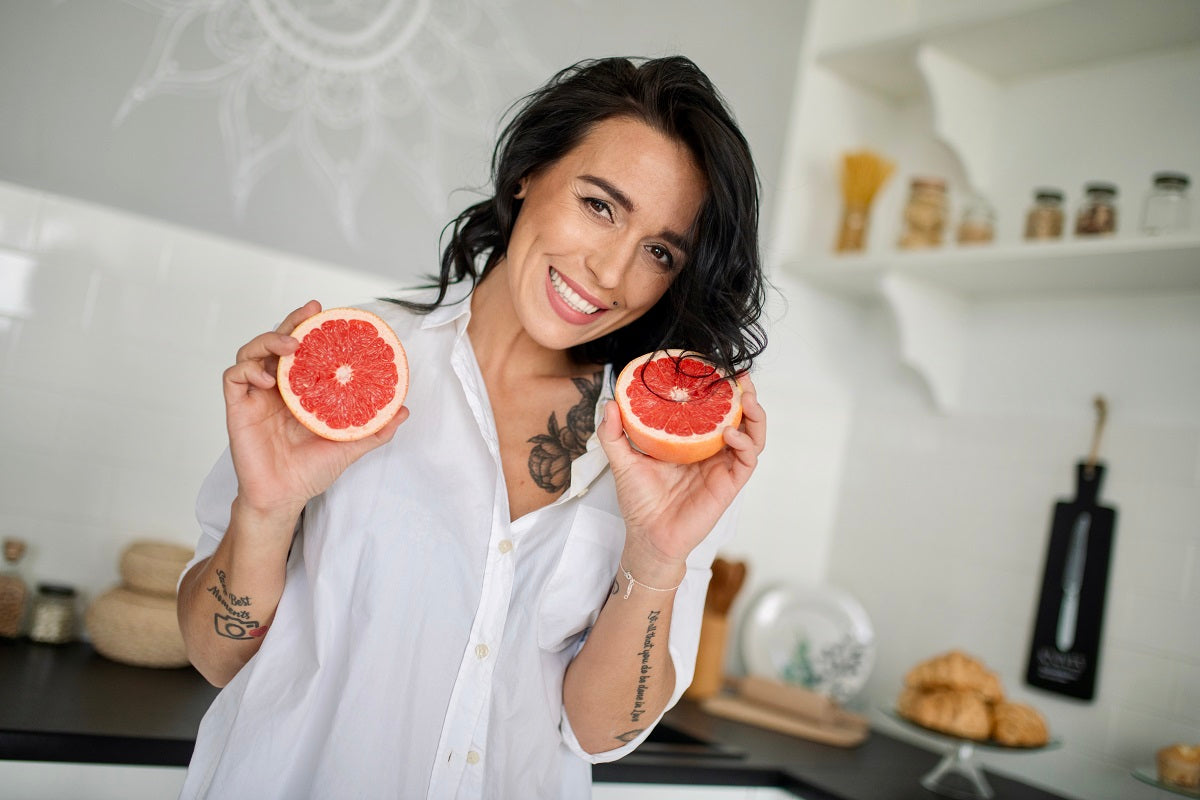 A woman smiling and holding a grapefruit cut in half
