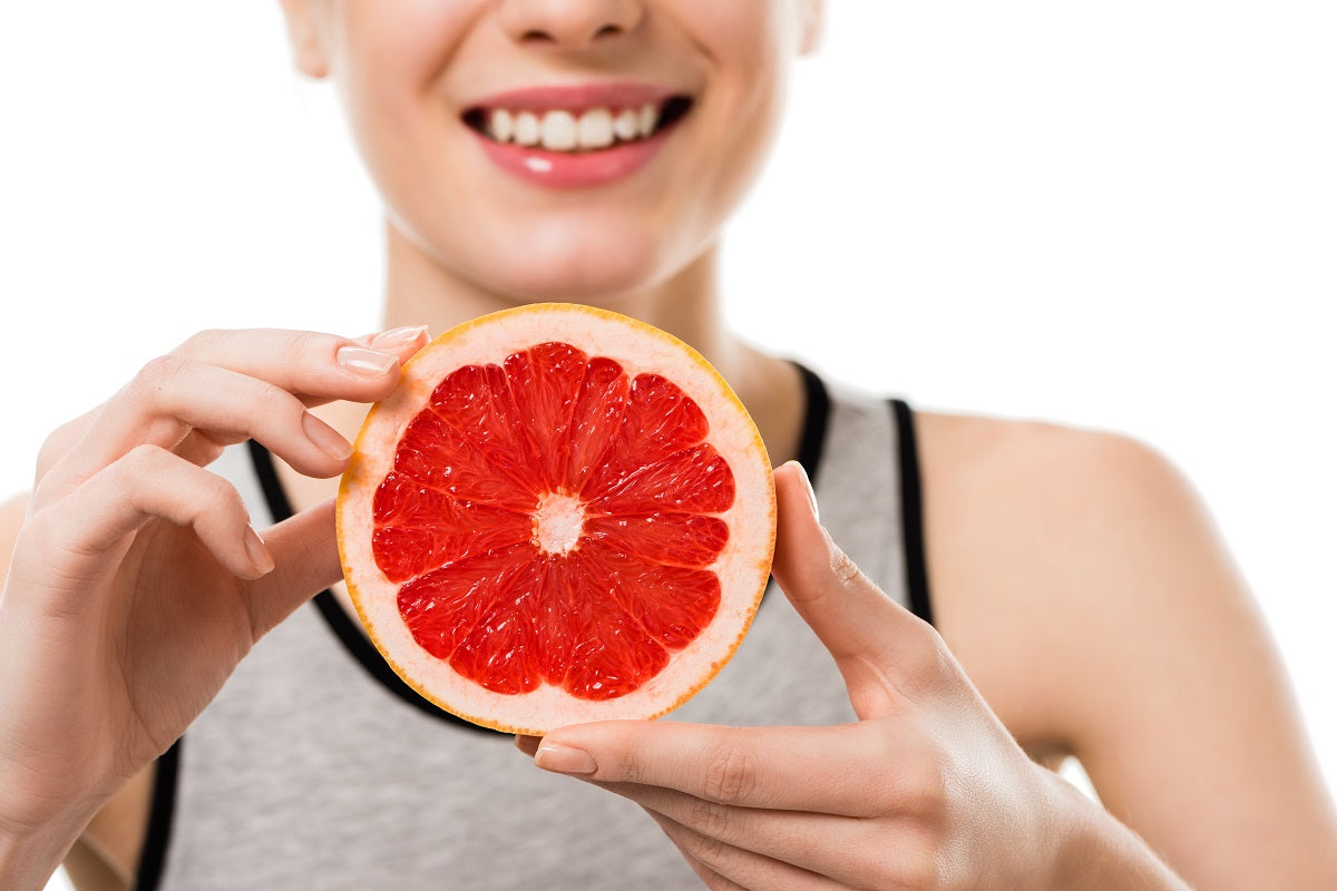A glass of grapefruit juice in front of a grapefruit cut into halves.
