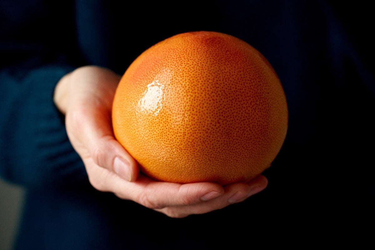 A person holding a grapefruit.