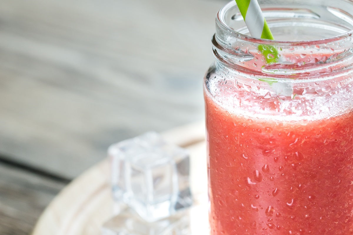 A glass filled with a red grapefruit smoothie on a round wooden tray.