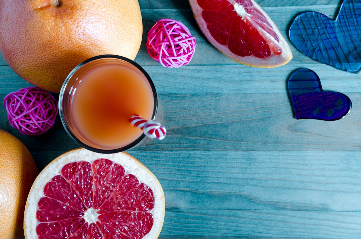 Fresh grapefruit juice in a clear glass with grapefruit slices and hearts on a blue wooden background.