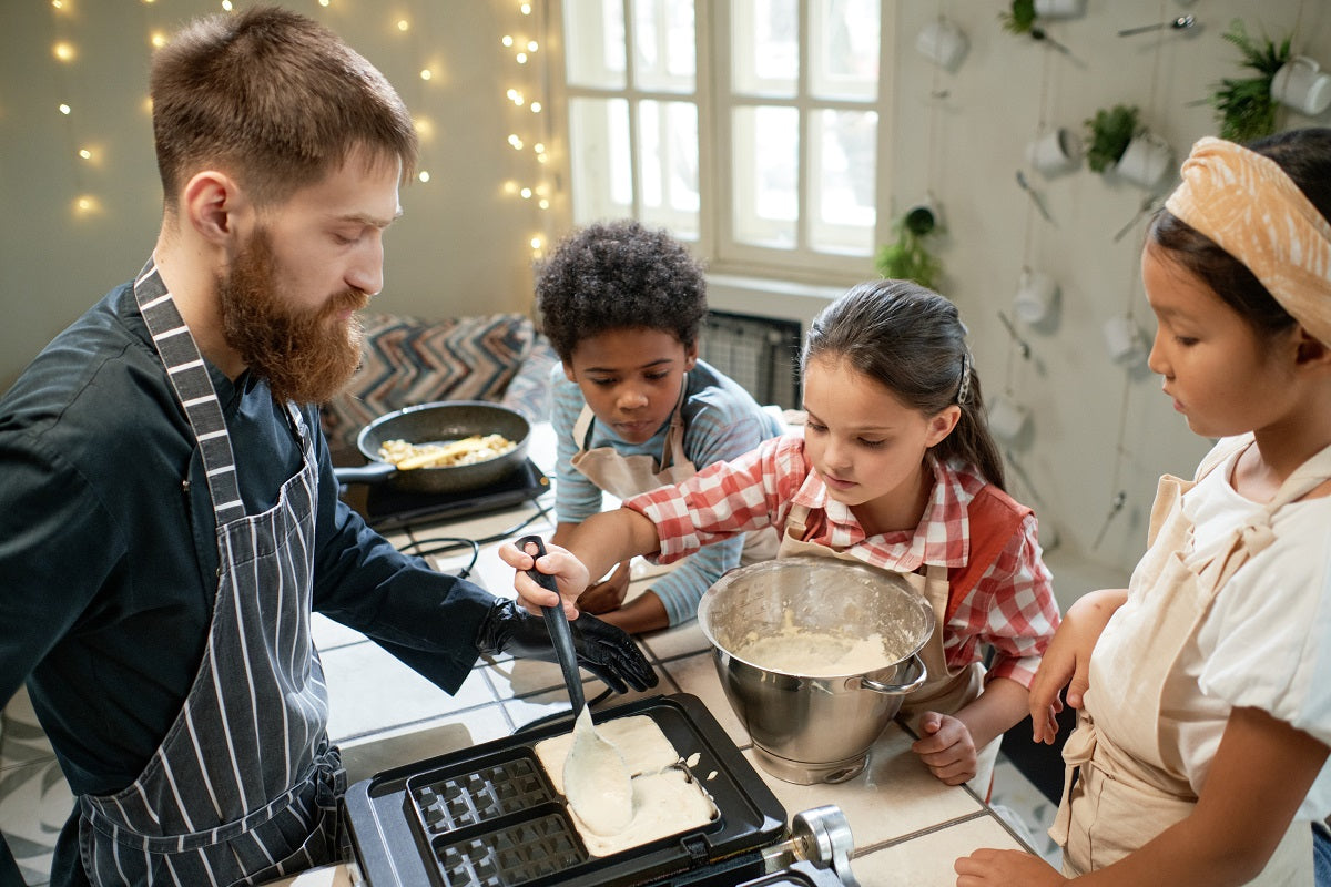 A group of children are learning to cook waffles with the help of a chef.