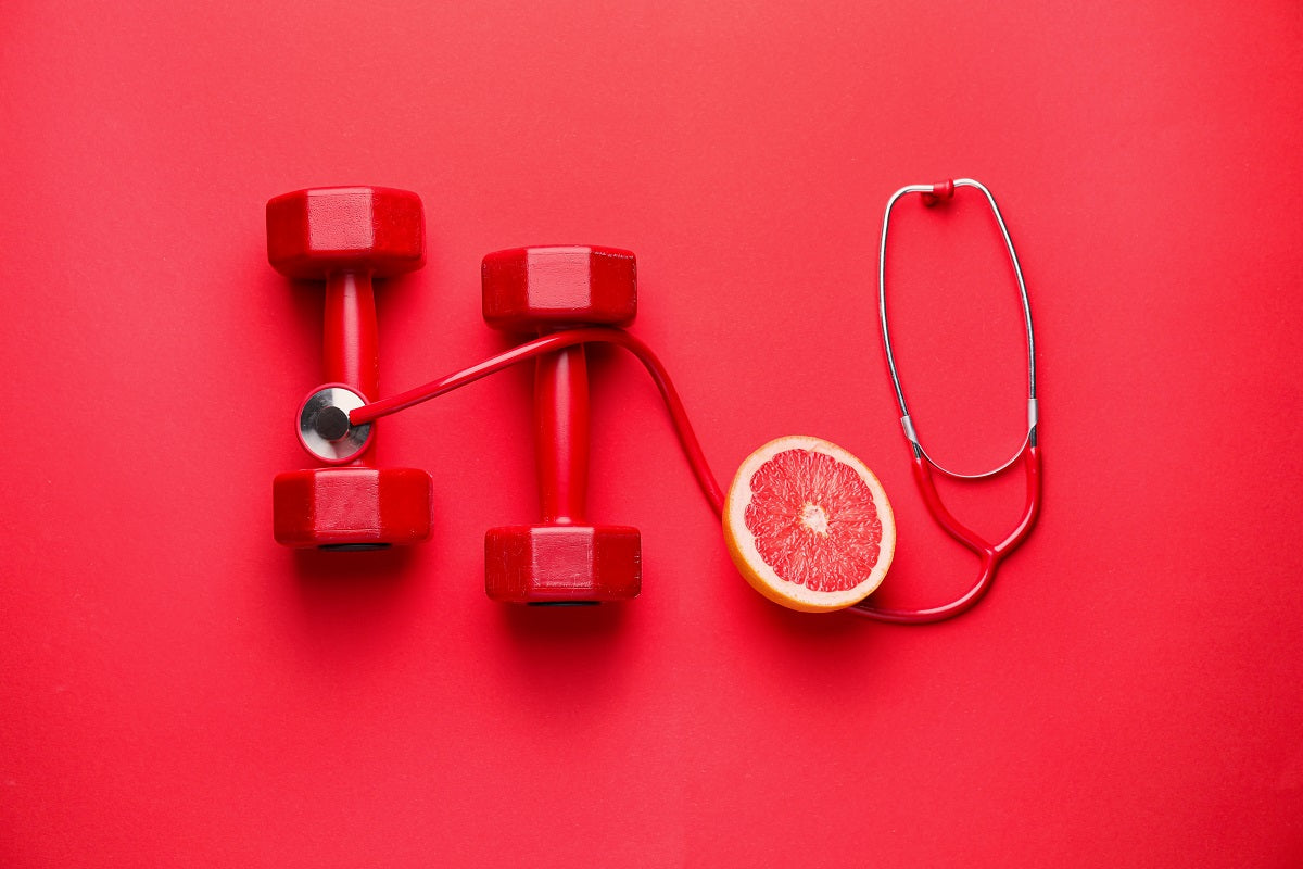 Two red dumbbells are on a red background with a stethoscope and a cut grapefruit.