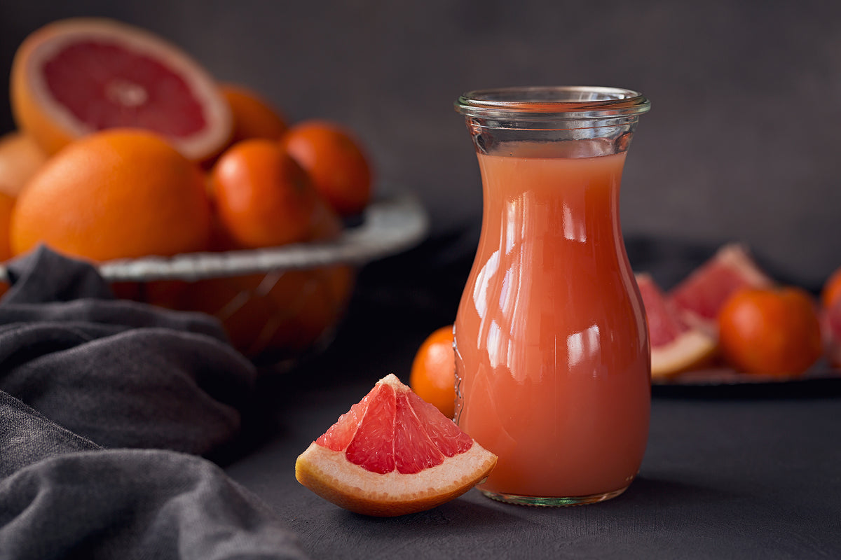 A glass of freshly squeezed grapefruit juice with some grapefruits in the background