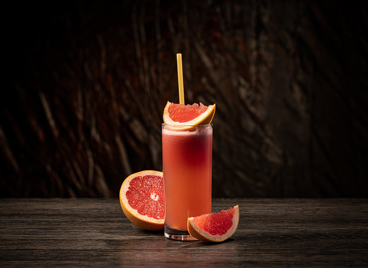 A glass filled with fresh grapefruit juice near a few grapefruit wedges